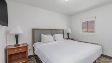 A hotel room with a large bed, two bedside tables with lamps, a flat-screen TV, a window with a view, and a carpeted floor.