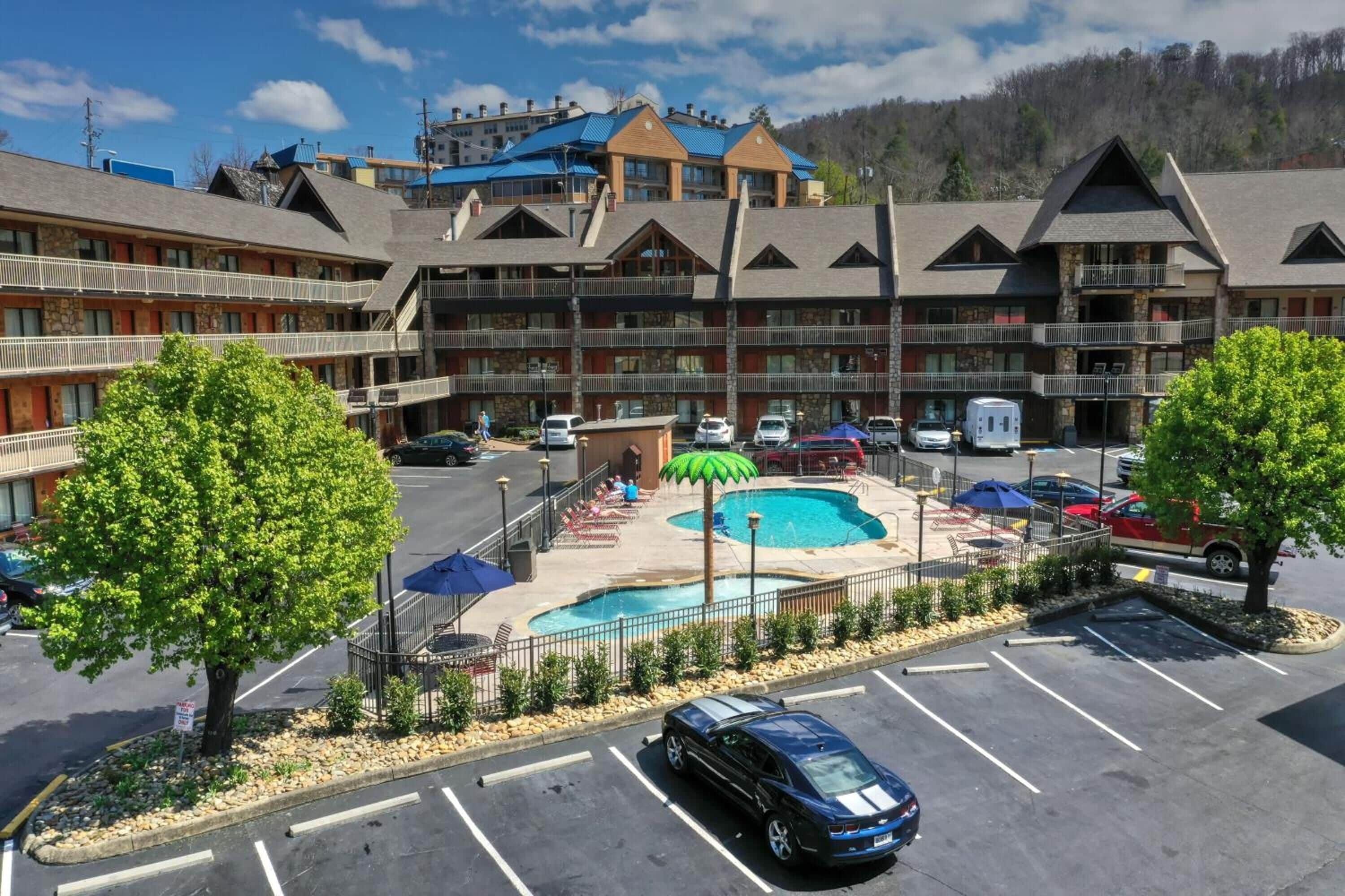 A multi-story hotel with a pool area, outdoor seating, and a parking lot.