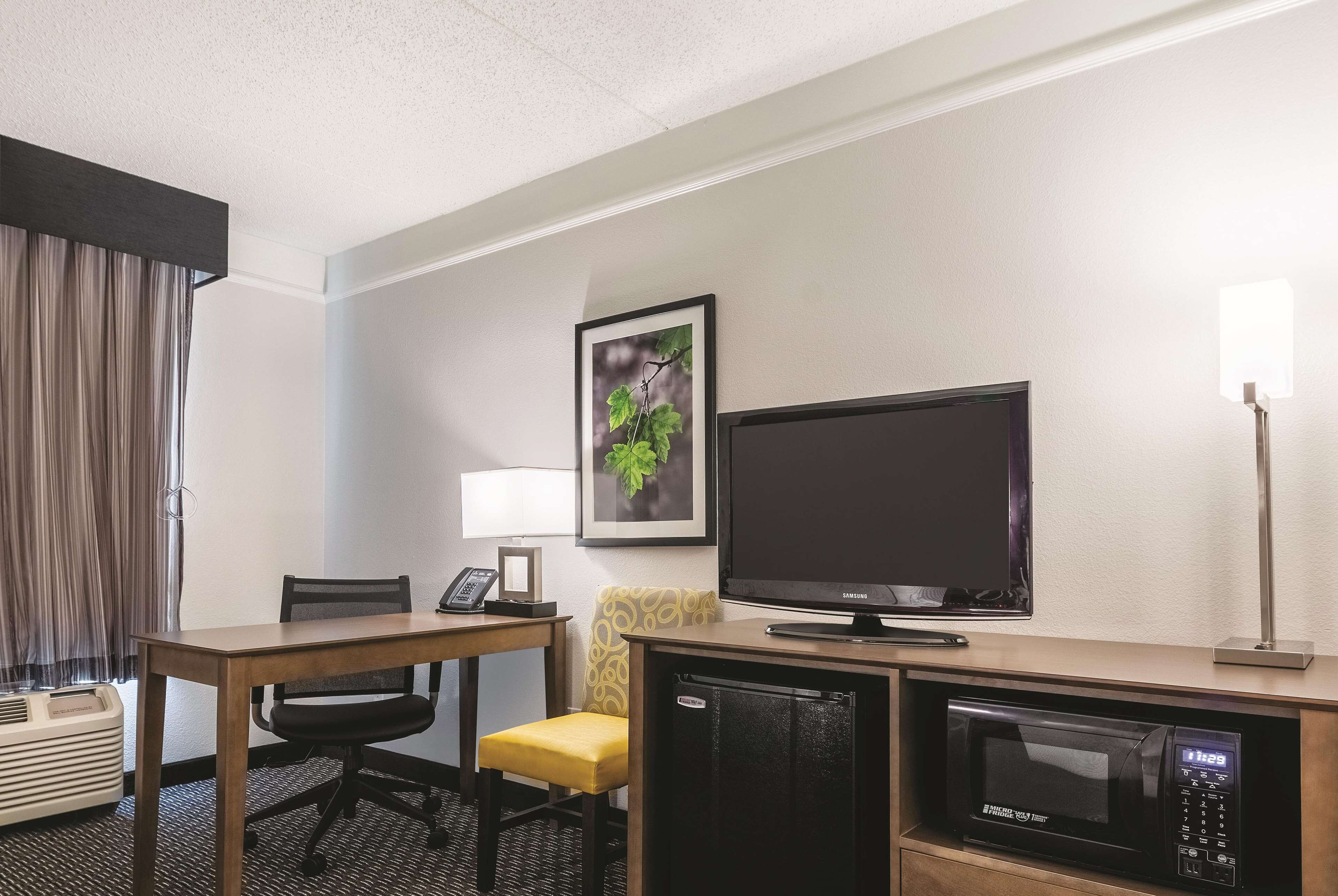 Habitación de hotel con un escritorio de madera, una silla amarilla, un televisor, un microondas y un cuadro en la pared.