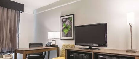 Habitación de hotel con un escritorio de madera, una silla amarilla, un televisor, un microondas y un cuadro en la pared.