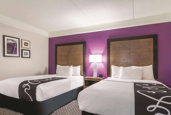 Una habitación de hotel con dos camas, una mesita de noche con lámpara y cuadros en la pared.