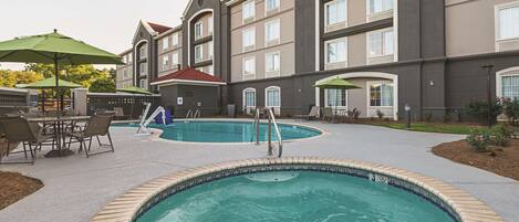 Un hotel con piscina, zona de estar al aire libre y un patio cubierto.