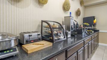 A kitchen area with a toaster, a bread display case, a coffee maker, and a waffle maker.