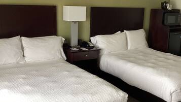 A hotel room with two beds, a nightstand, a lamp, a TV, and a minibar.