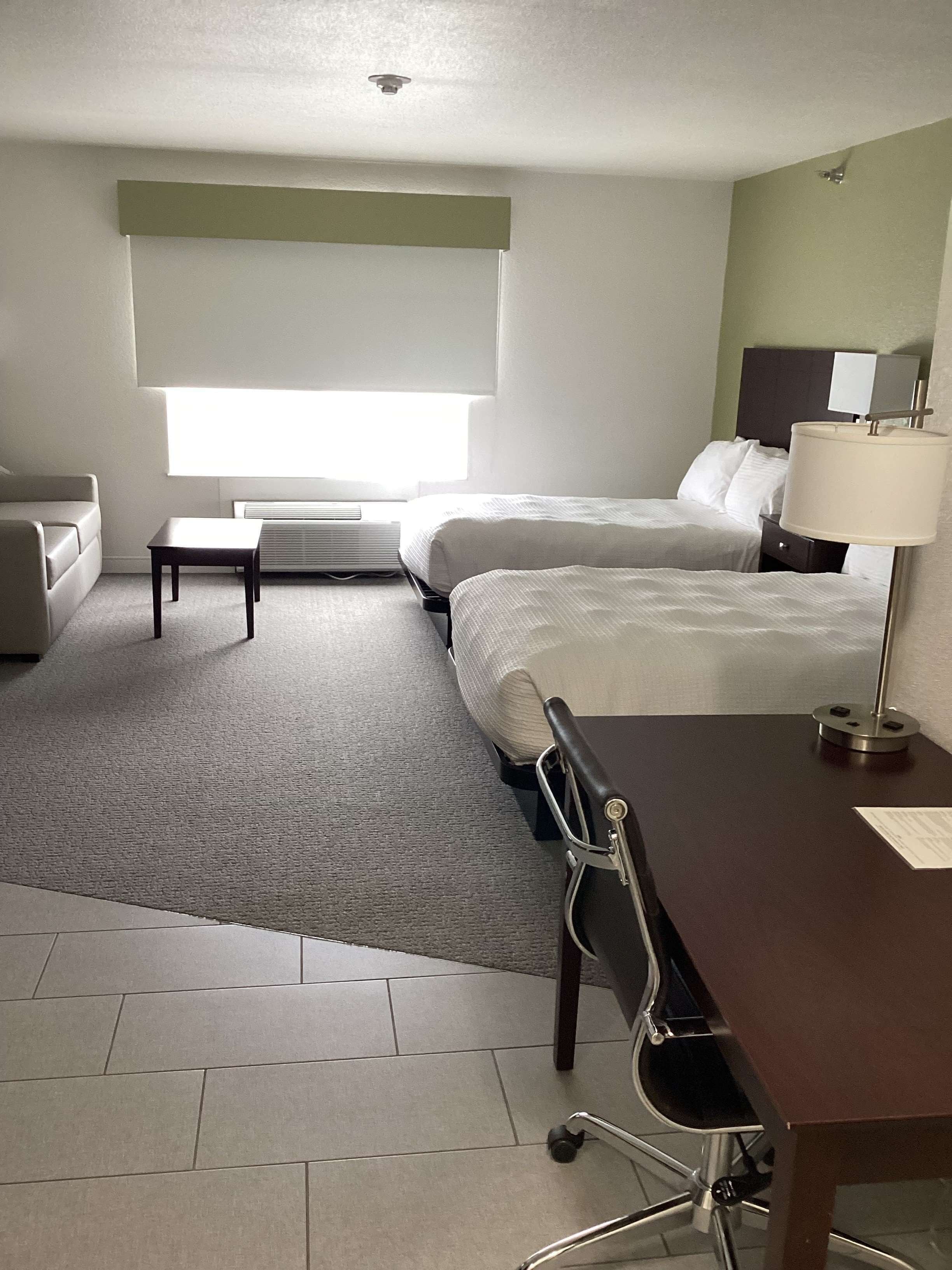 A hotel room with a bed, a desk, a chair, a lamp, and a window.
