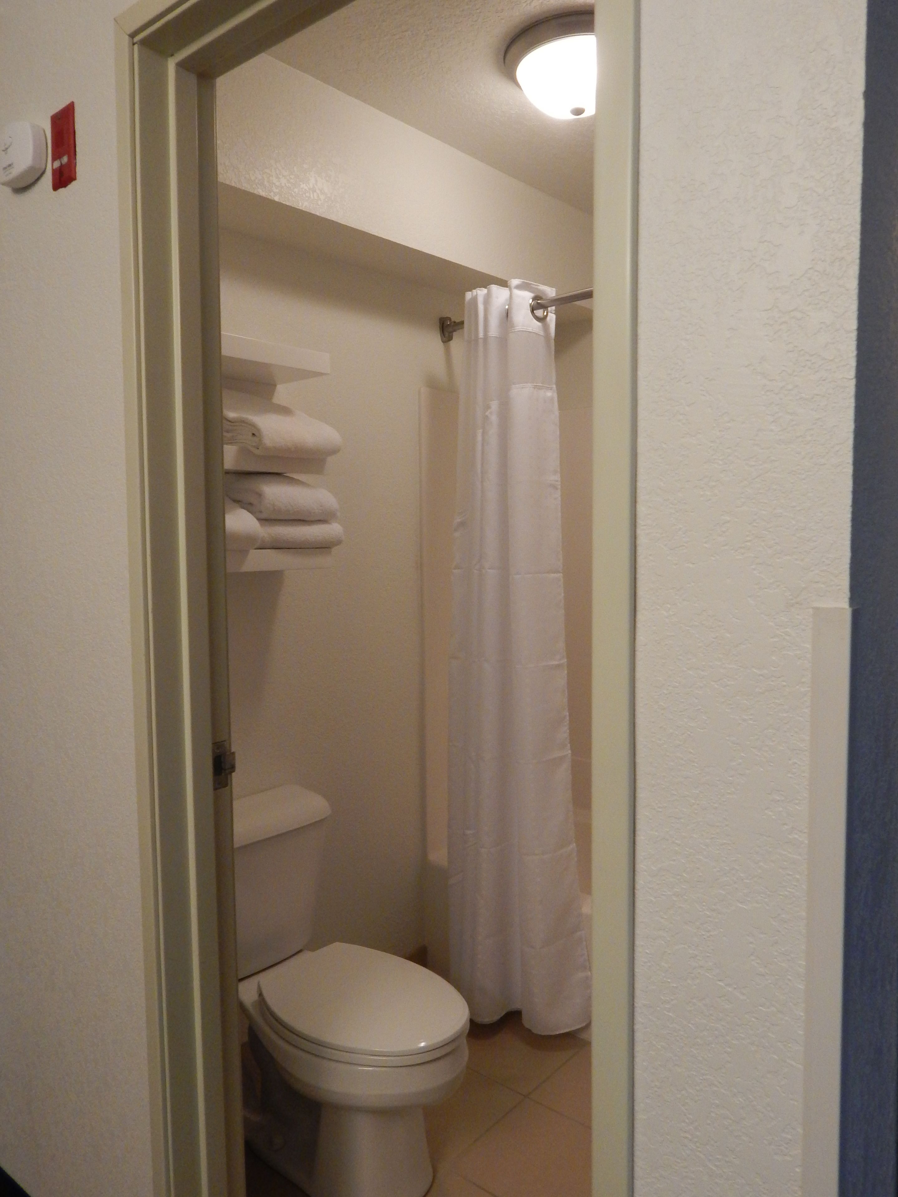 Un baño con inodoro, cortina de ducha y una pila de toallas blancas.