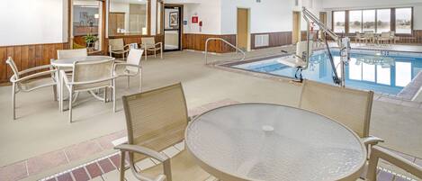 An indoor pool area with a glass table and chairs, a pool ladder, and a view of the beach through large windows.