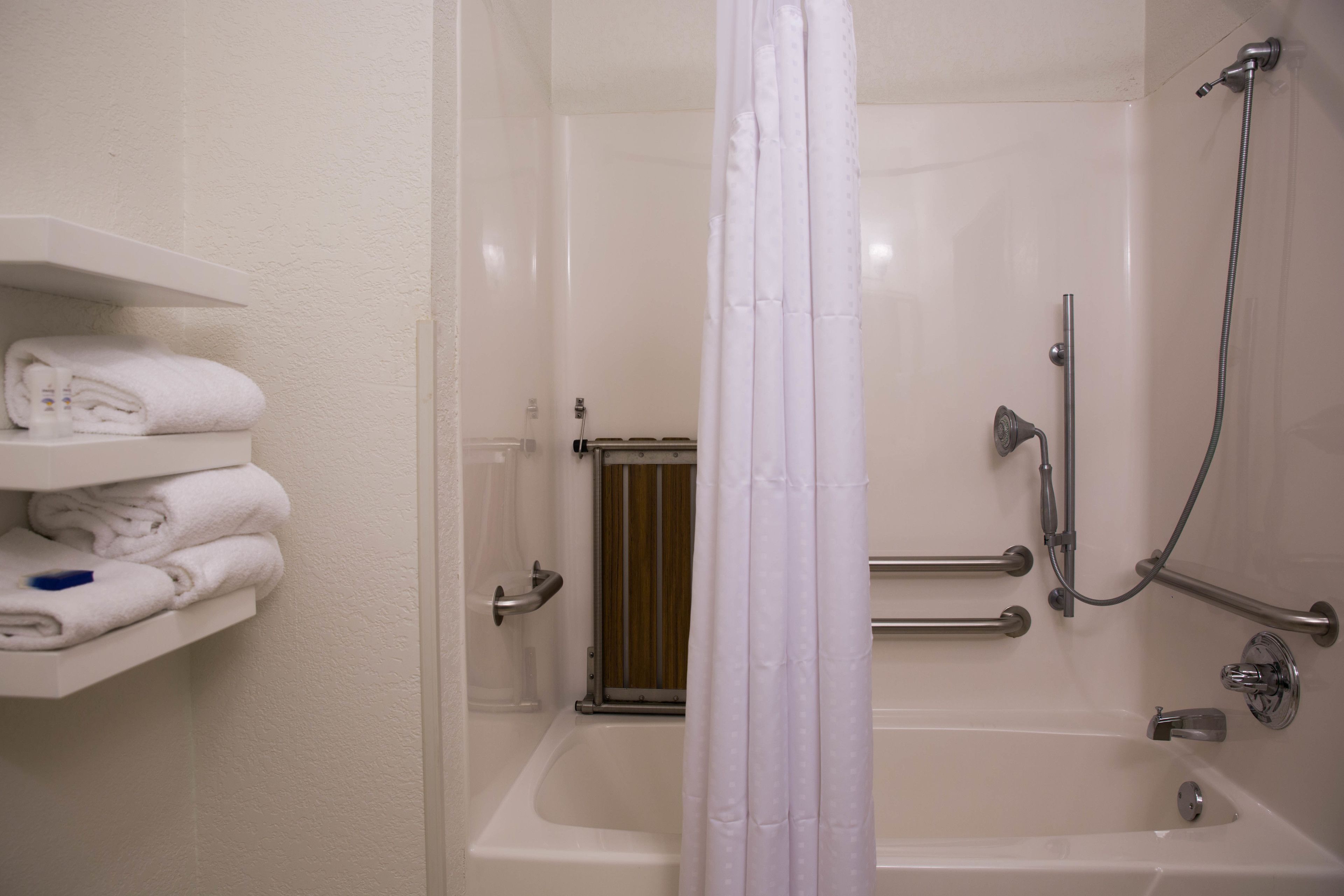 A bathroom with a bathtub, a shower, and a shelf with folded towels.
