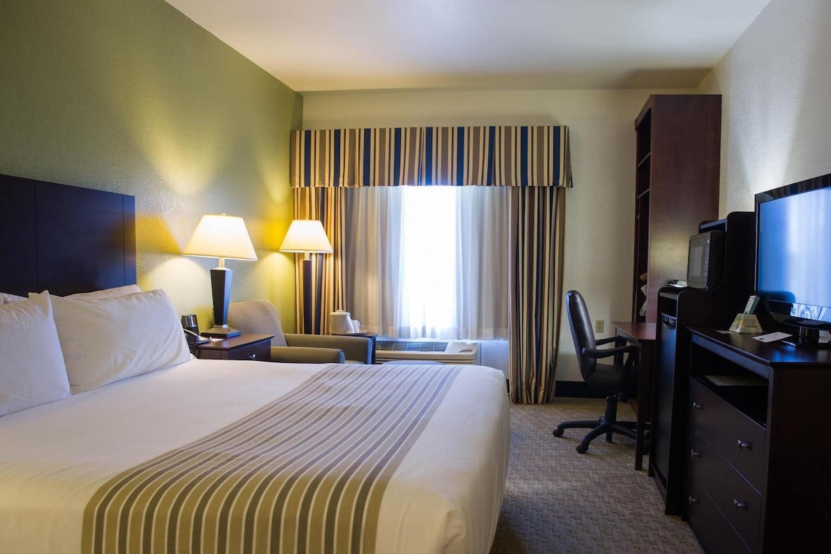 A hotel room with a large bed, two bedside lamps, a desk with a computer, a chair, and a television.