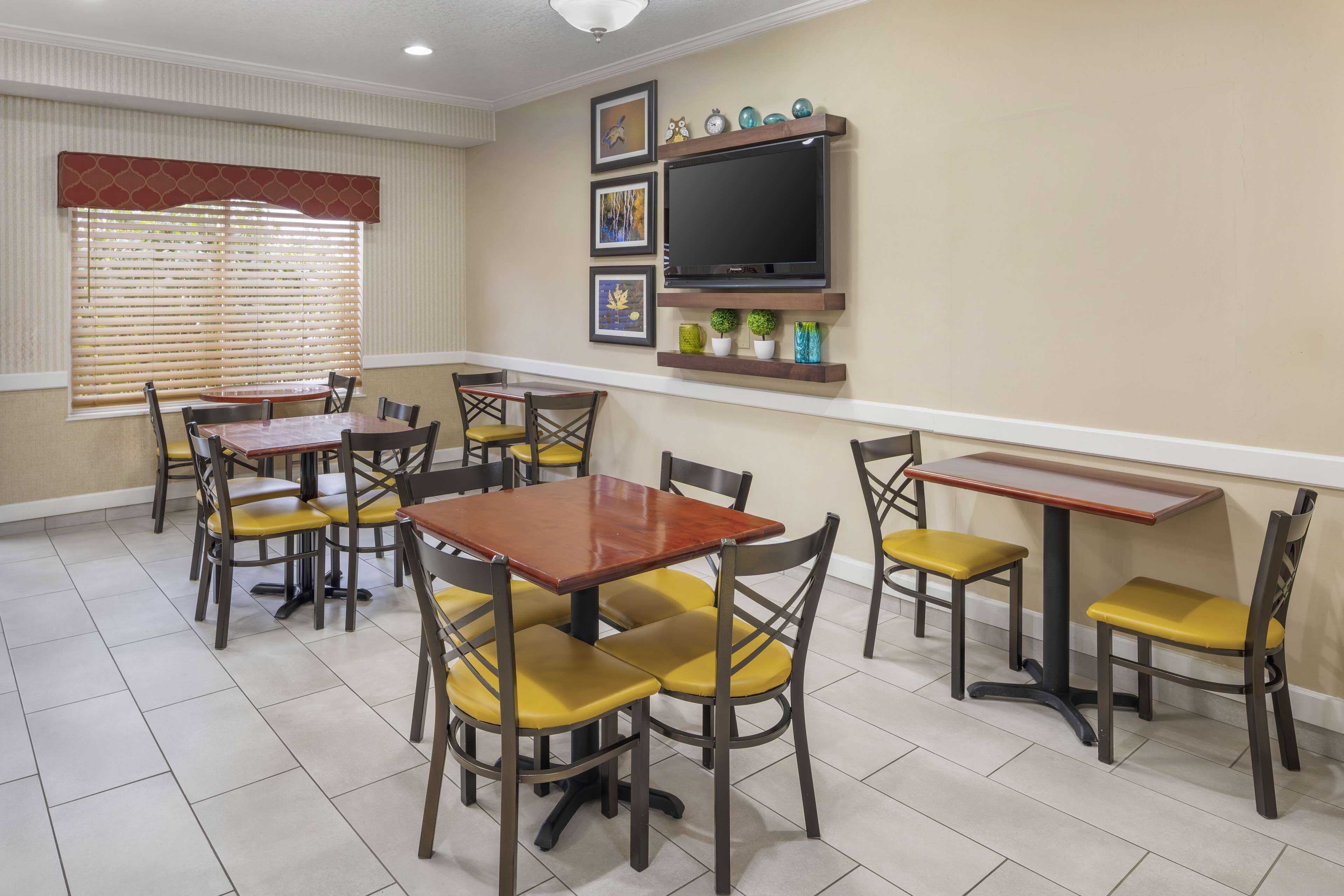 A dining area with multiple tables and chairs, a television mounted on the wall, and framed artwork above the TV.