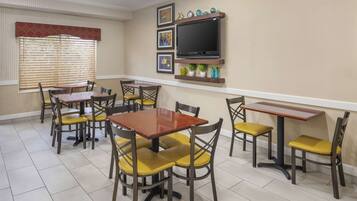 A dining area with multiple tables and chairs, a television mounted on the wall, and framed artwork above the TV.