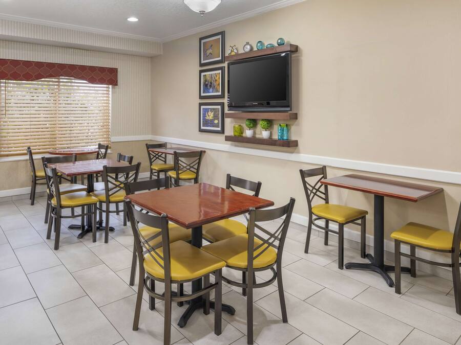 A dining area with multiple tables and chairs, a television mounted on the wall, and framed artwork above the TV.
