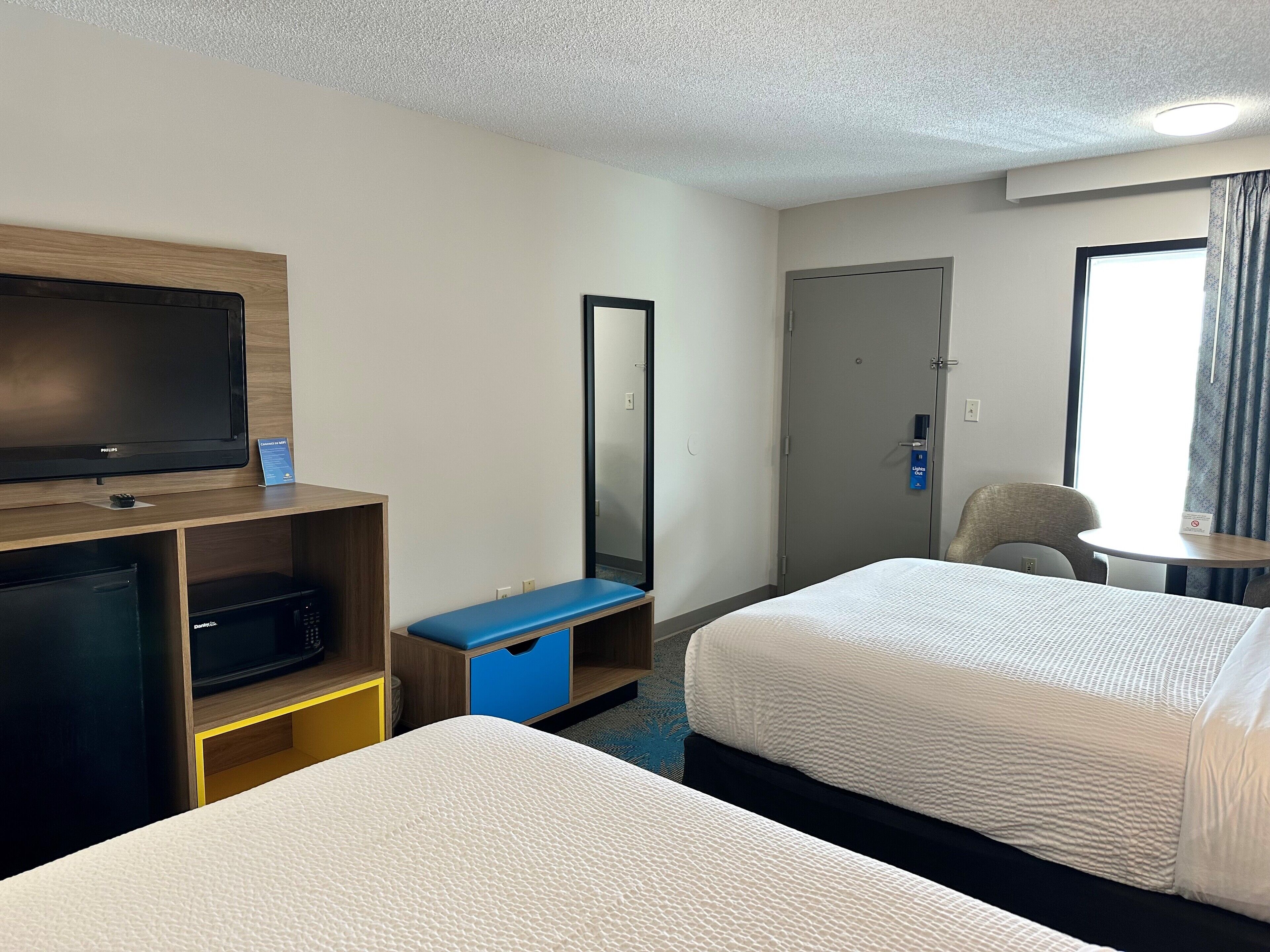 A hotel room with a bed, a desk with a television, a mirror, a wardrobe, and a door.