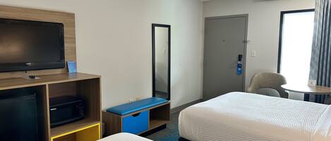 A hotel room with a bed, a desk with a television, a mirror, a wardrobe, and a door.