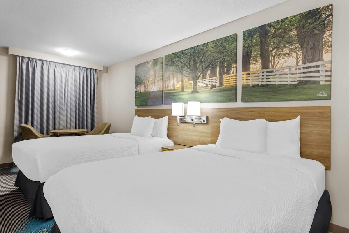 Ett hotellrum med två sängar, ett skrivbord, en stol och ett stort fönster med gardiner.