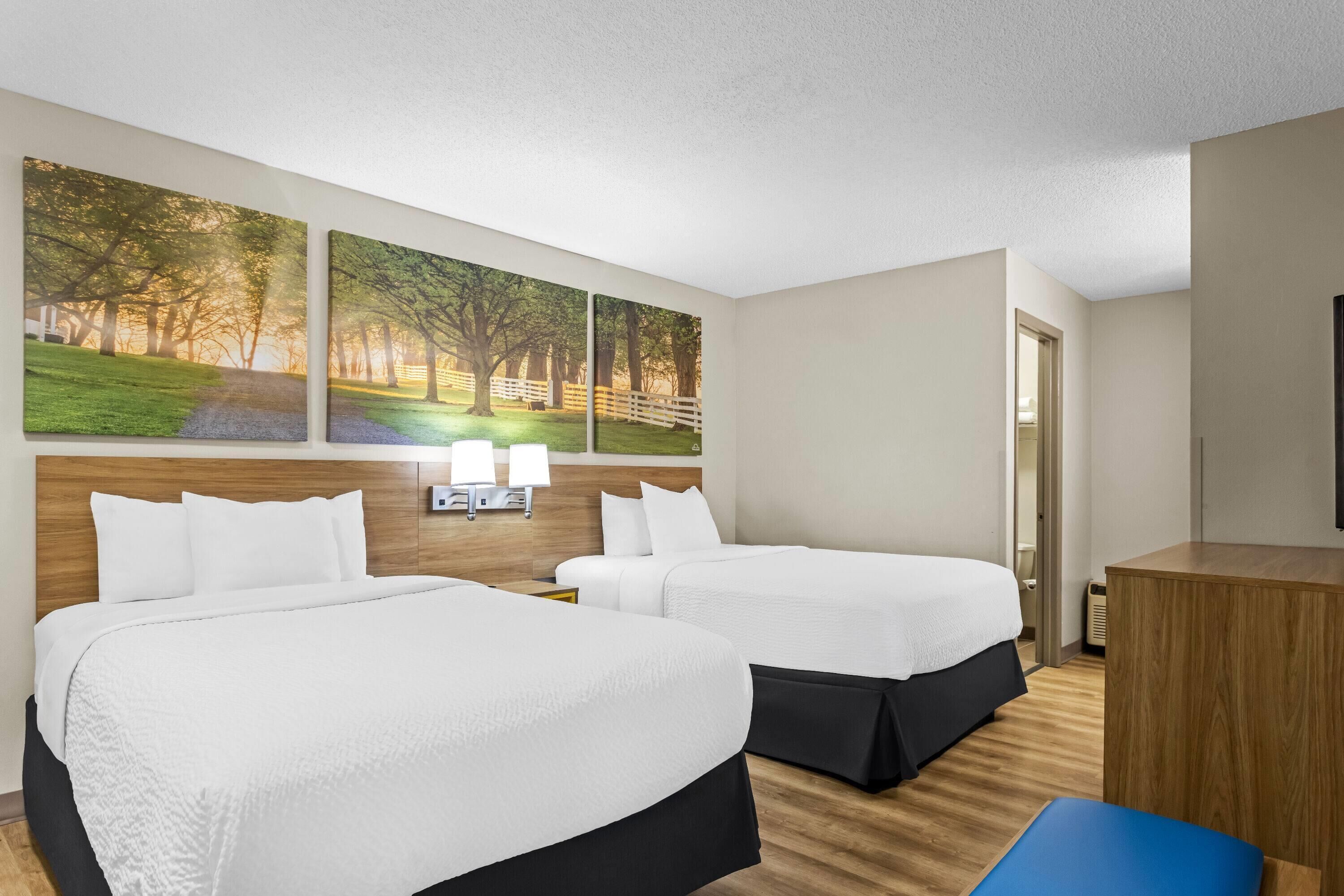 A hotel room with two beds, a desk, and a wall-mounted lamp.