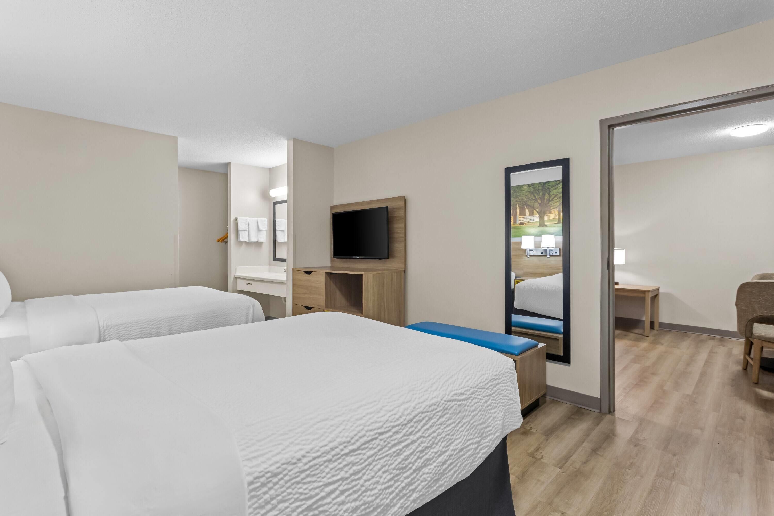 A hotel room with two beds, a desk, a television, and a mirror.
