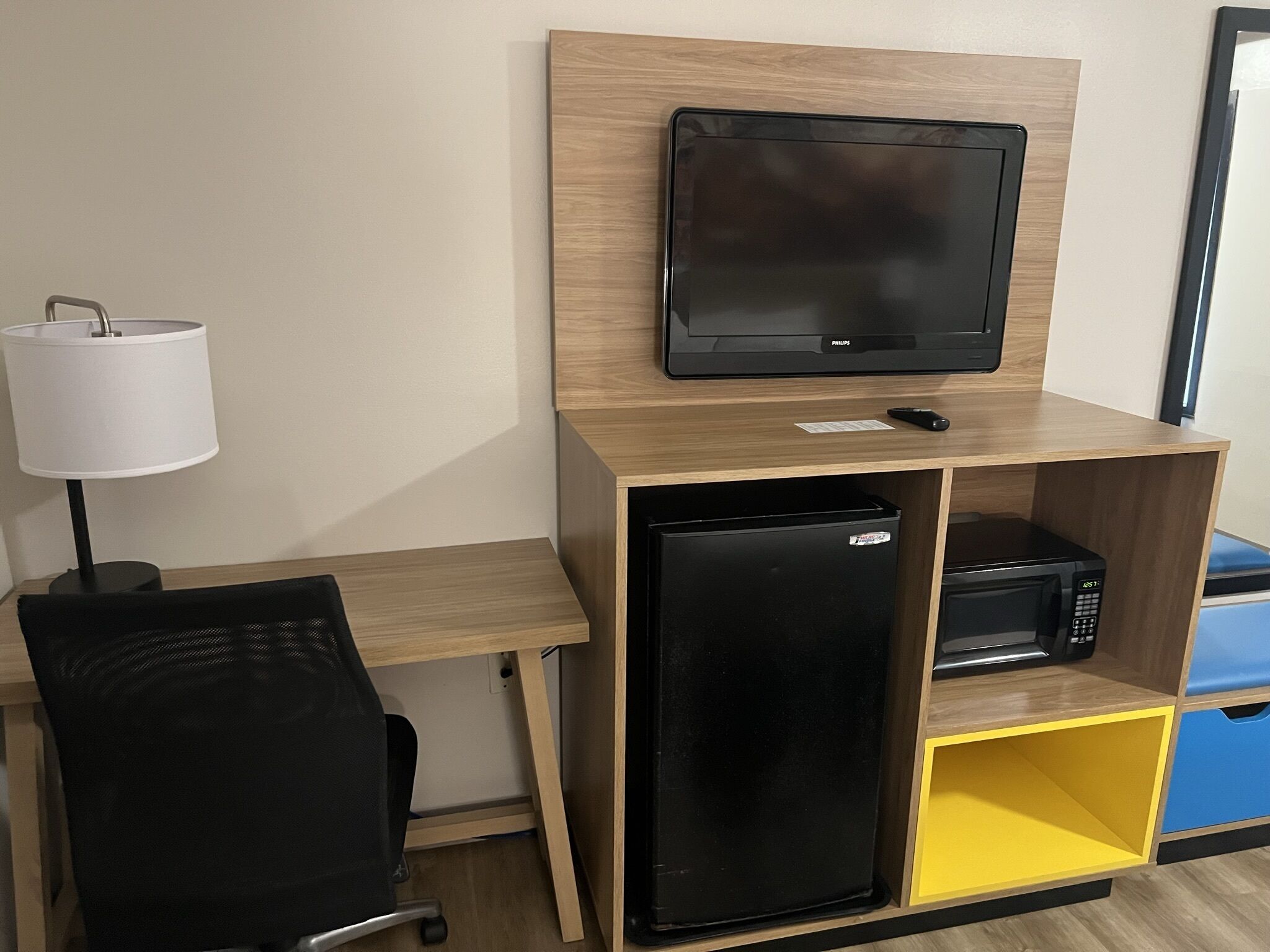 A compact room with a wooden desk, a black refrigerator, a microwave, a television, and a chair.