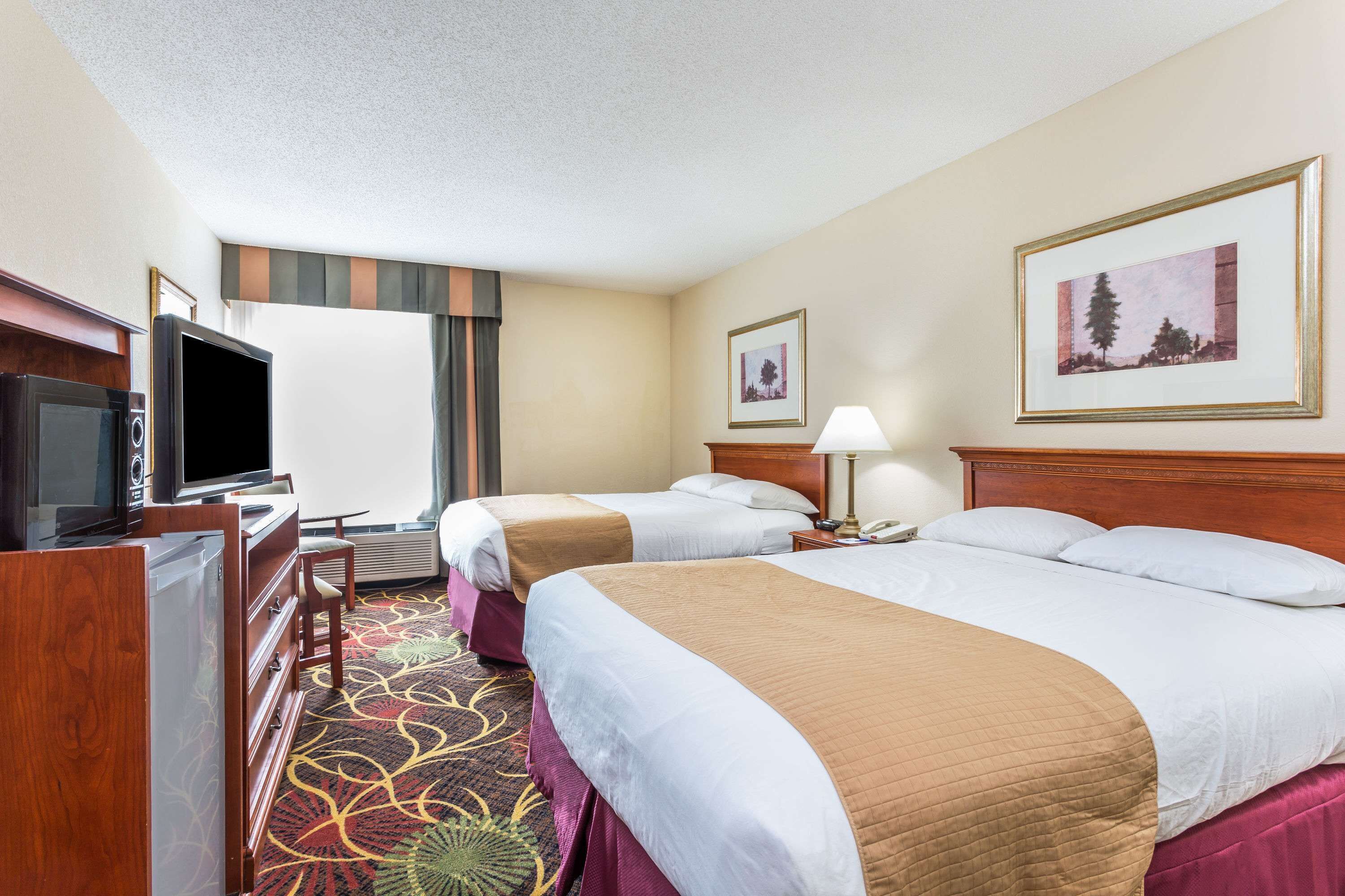 A hotel room with two beds, a television, a desk, and a large window.