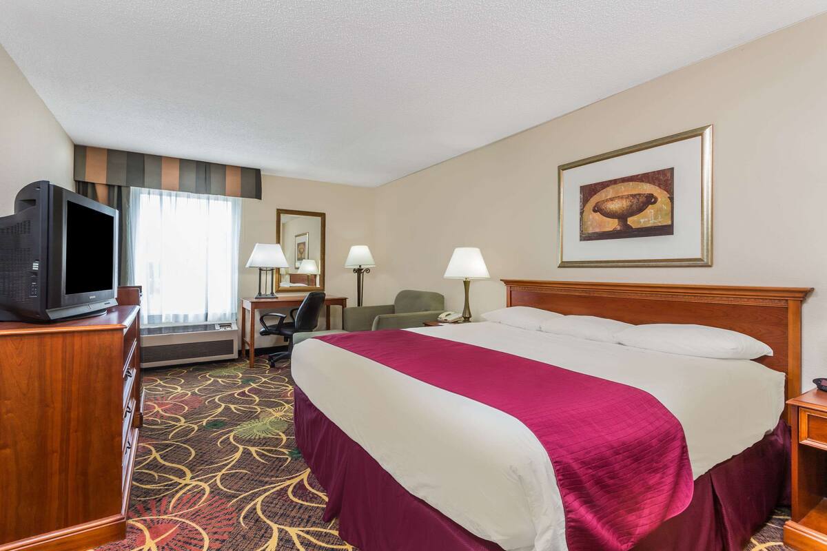 A hotel room with a large bed, a television on a wooden cabinet, a desk with a chair, and a framed picture on the wall.