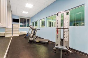 Un gimnasio hotelero con cinta de correr, máquinas de pesas y espejos en las paredes.