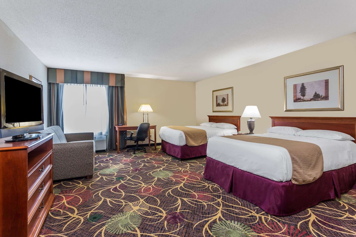 A hotel room with a large bed, two smaller beds, a desk with a chair, a television, and a carpeted floor.