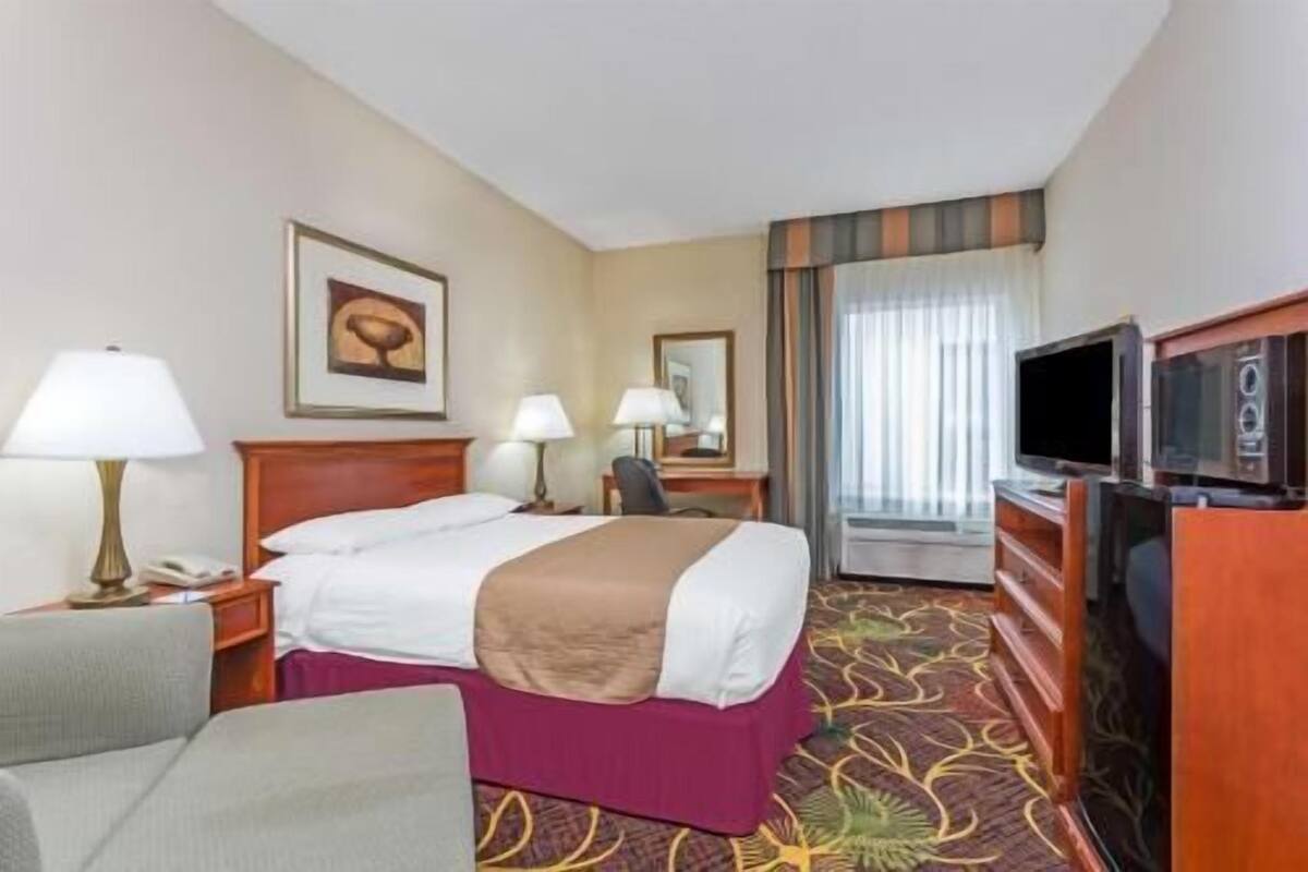 A hotel room with a bed, two bedside lamps, a television, a desk, and a chair.