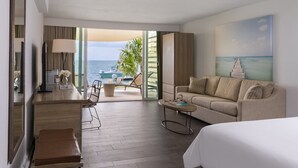 Habitació d'hotel amb llit, sofà, taula de cafè, escriptori amb làmpada i vista a l'oceà.