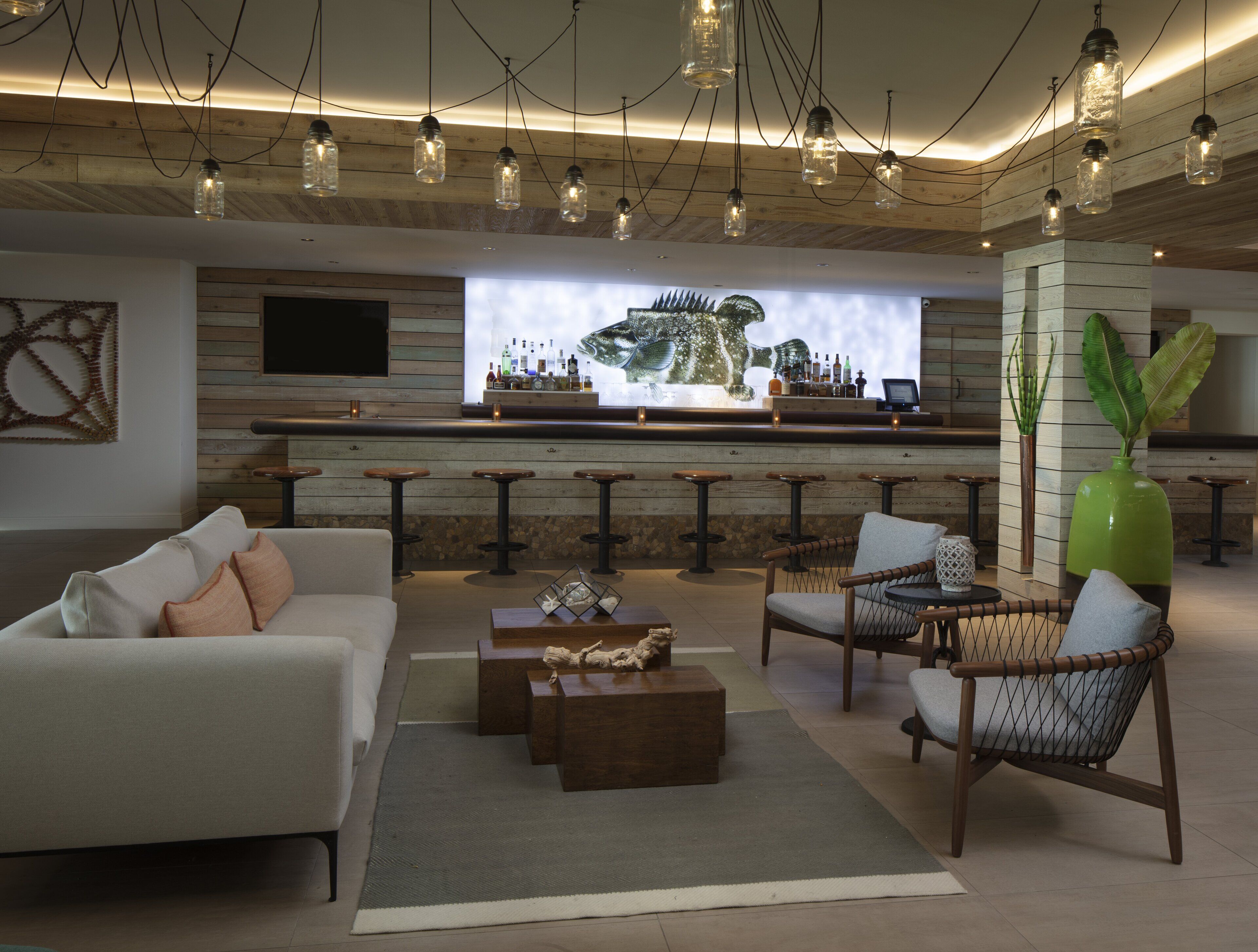 A modern bar area with a wooden bar counter, multiple stools, and a television screen displaying a bar scene.