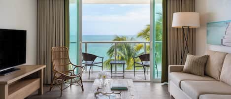 A modern hotel room with a balcony, a TV, a sofa, a coffee table, and a view of the ocean.