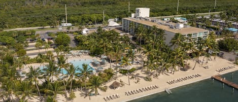 An aerial view of a resort with a beach, pool, and palm trees.