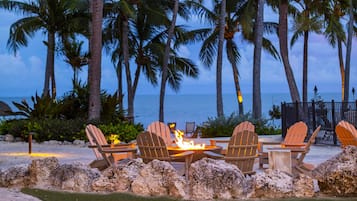 Un patio frente a la playa con mesas al aire libre, palmeras y vistas al océano.