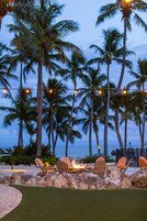 Un patio frente a la playa con mesas al aire libre, palmeras y vistas al océano.