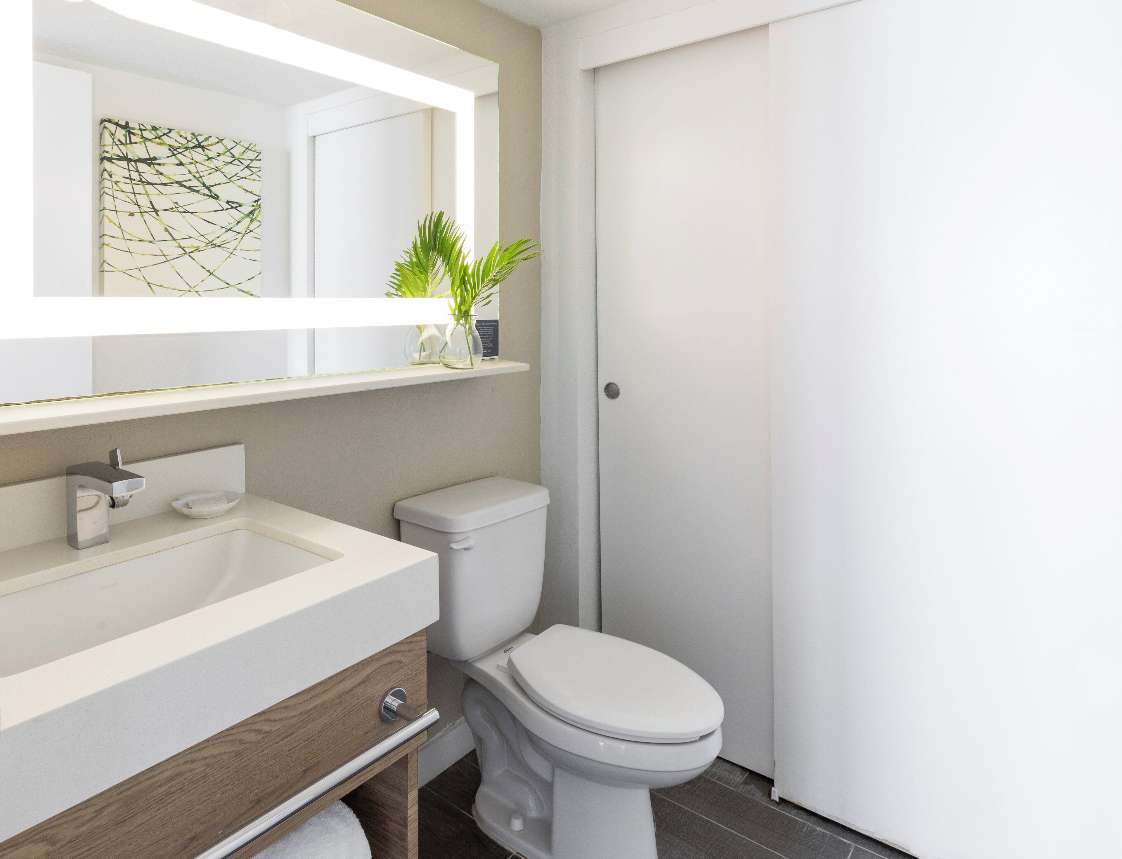 A modern bathroom with a white sink, a toilet, and a mirror above the sink.