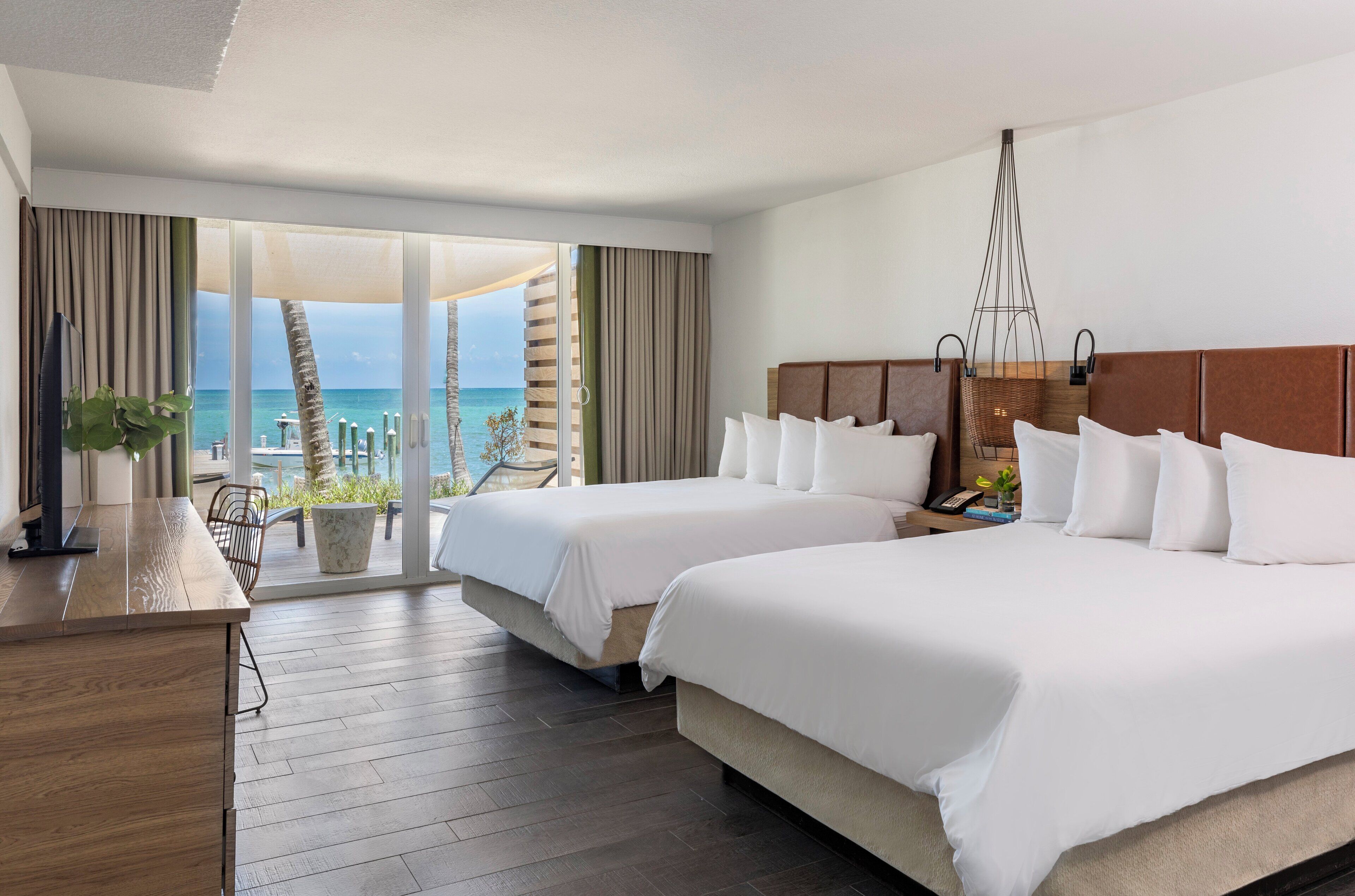 Habitación de hotel con dos camas, un escritorio y un ventanal con vistas al océano.