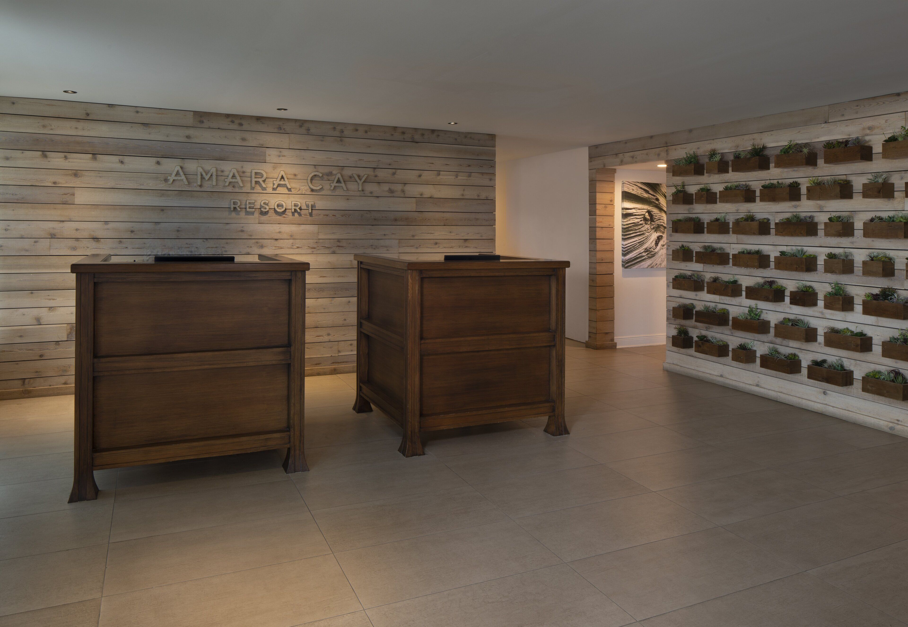 Un área de recepción con paneles de madera, un mostrador de recepción y una pared llena de plantas en macetas.