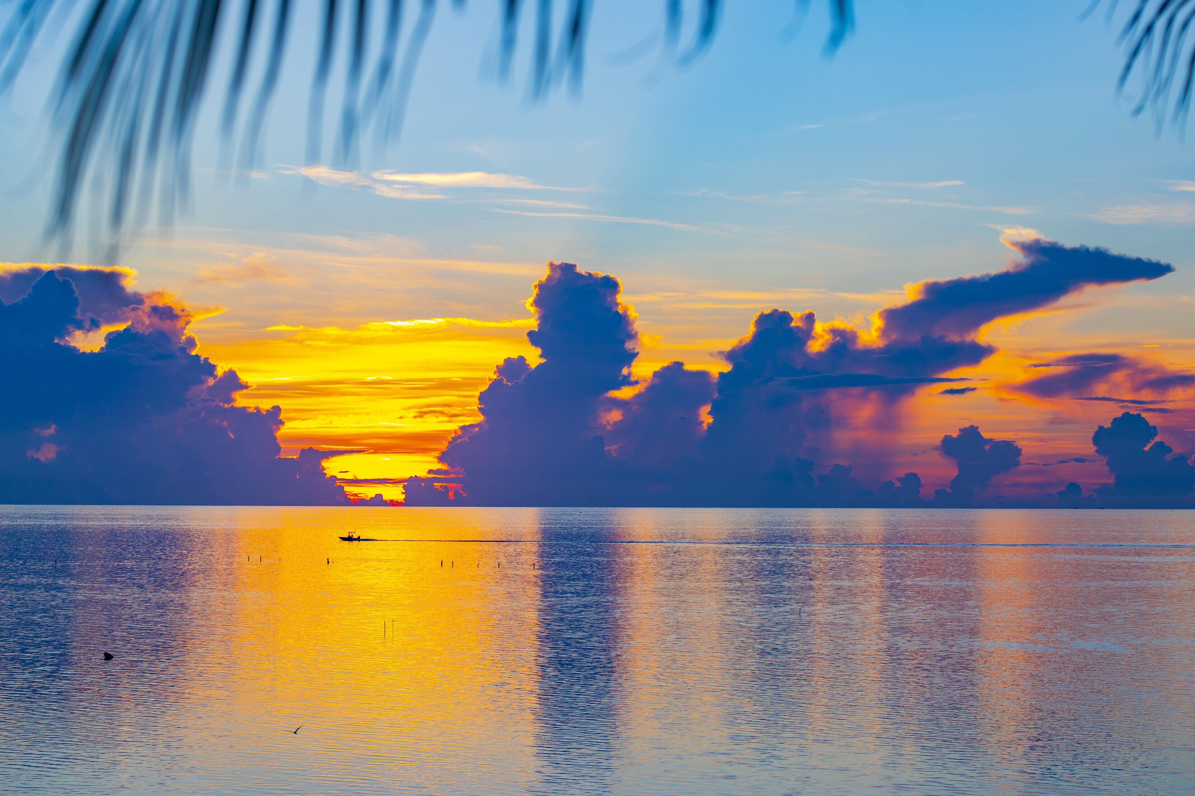 A sunset over a calm sea with a boat in the distance.
