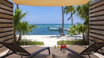 A wooden deck with two lounge chairs, a table with drinks and flowers, and a view of the beach and ocean.