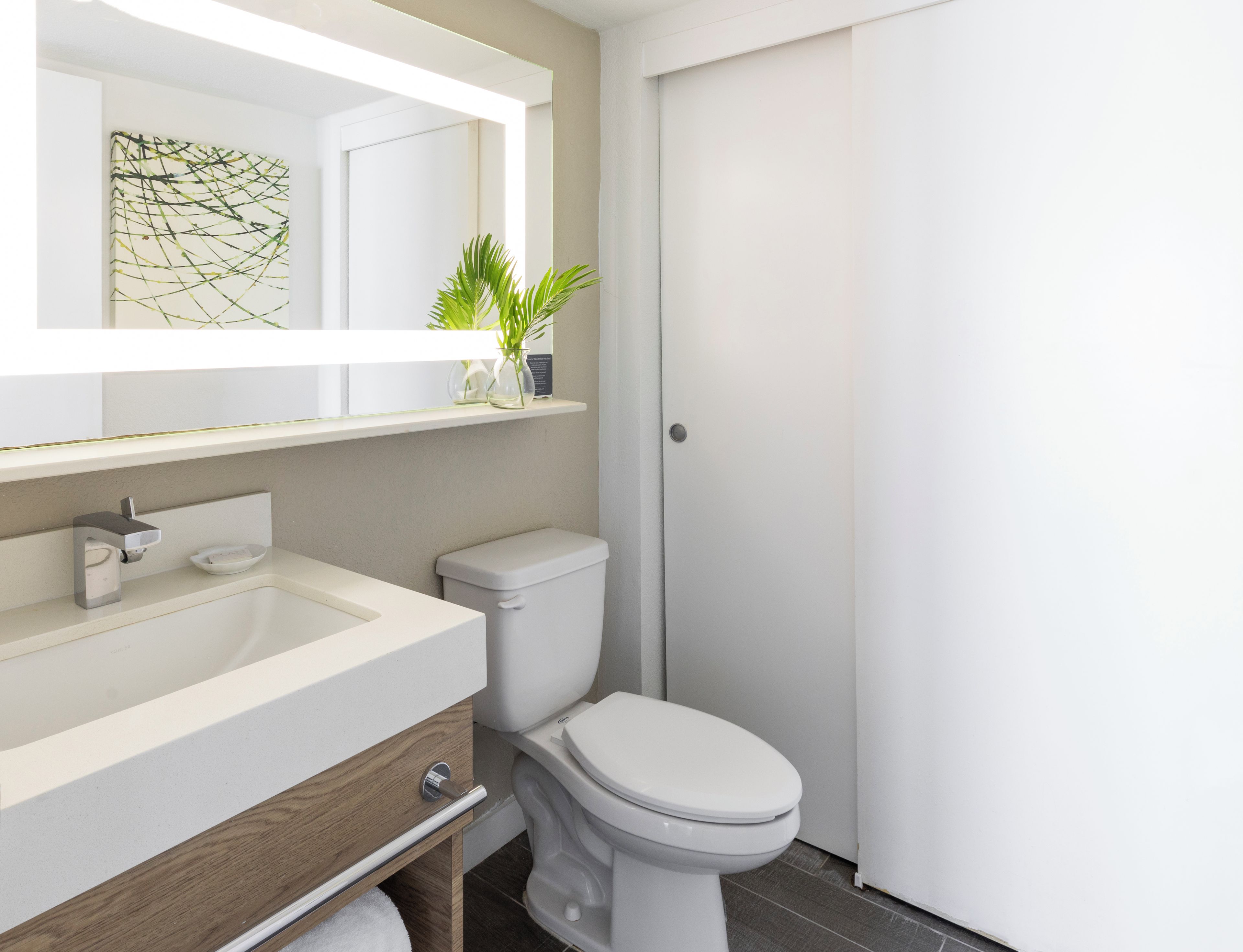 Un baño moderno con un lavamanos blanco, un inodoro y un espejo sobre el lavamanos.