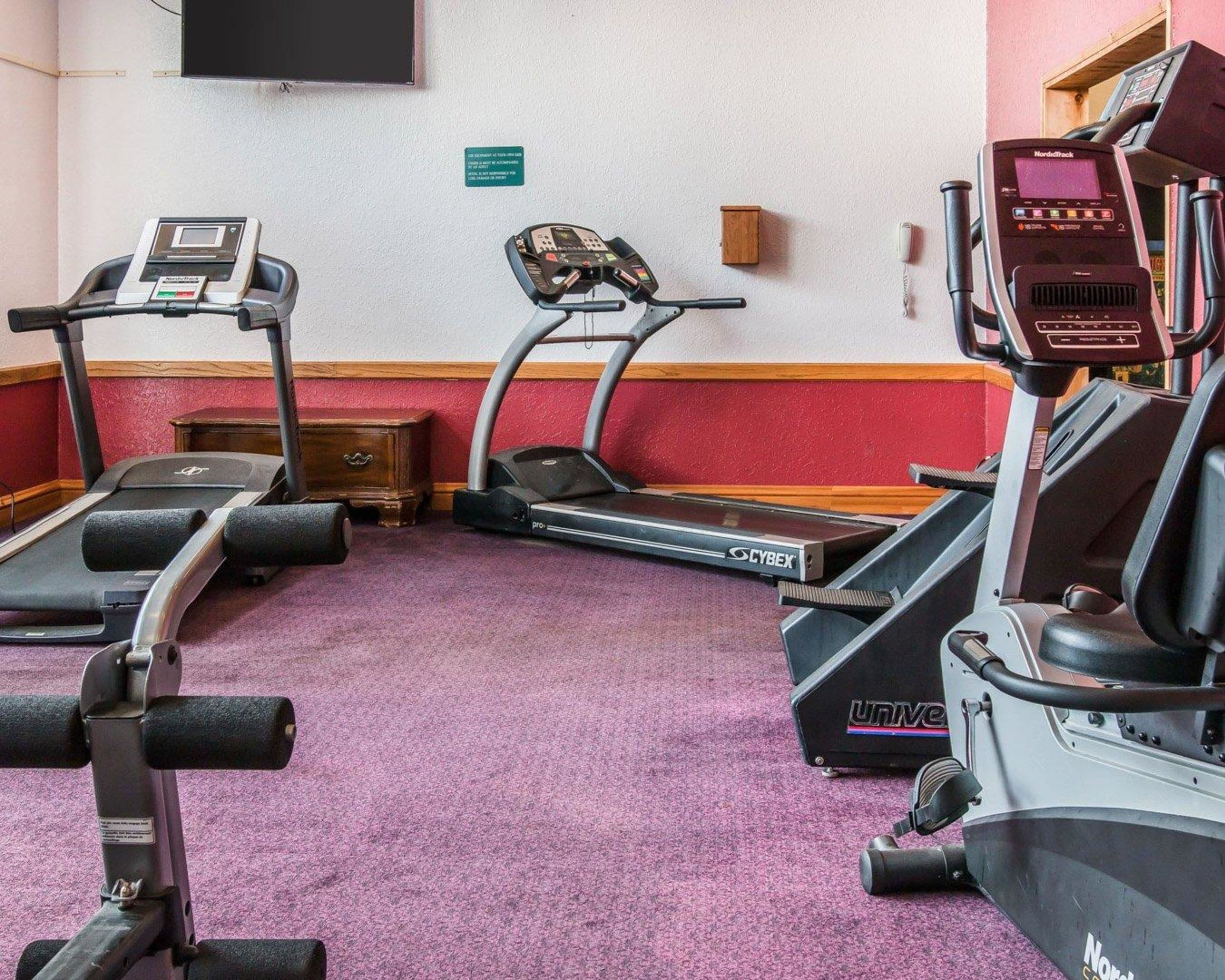 Een fitnessruimte met loopbanden, een hometrainer en een gewichtbank.