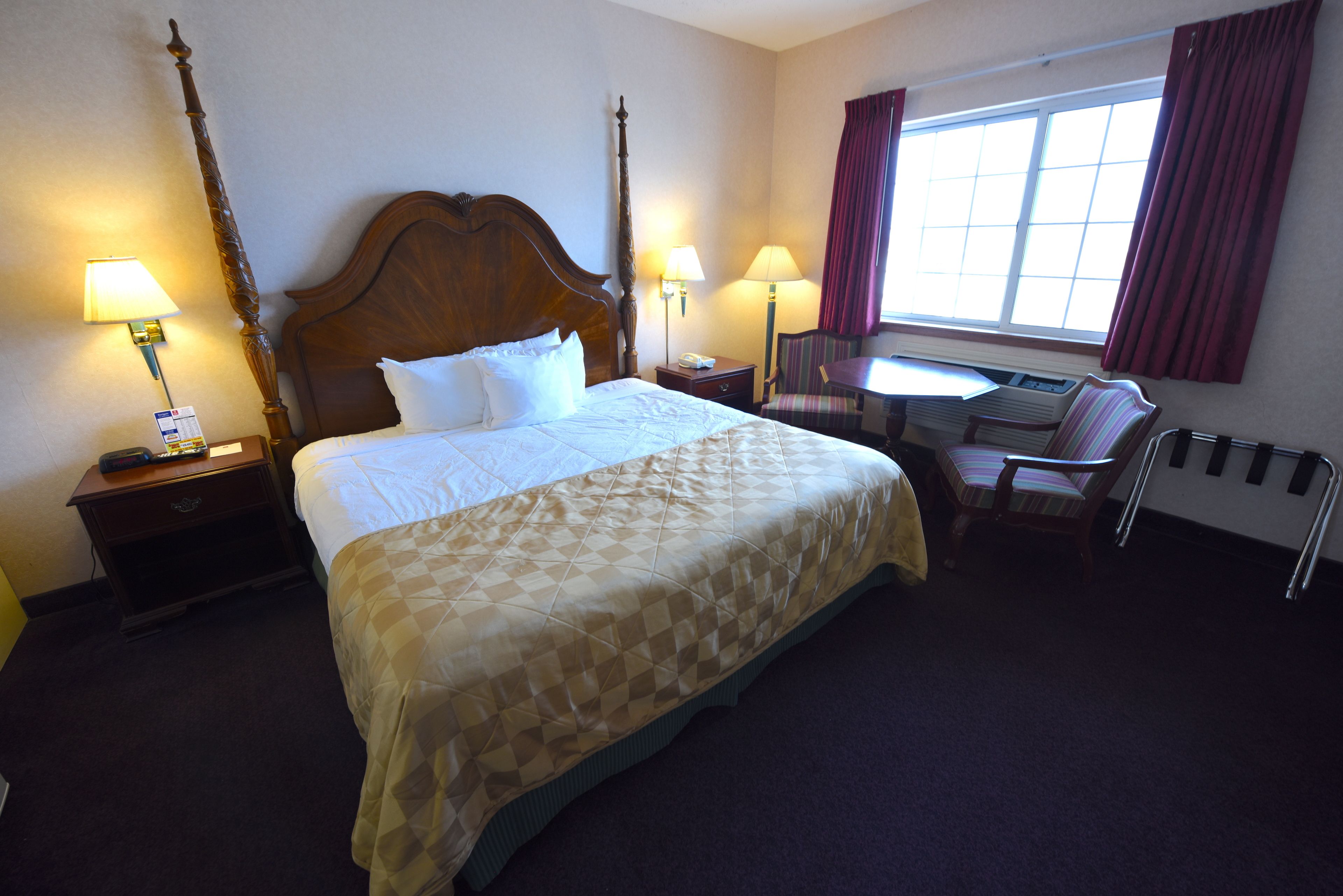 A hotel room with a large bed, two bedside tables with lamps, a desk with a chair, and a window with curtains.