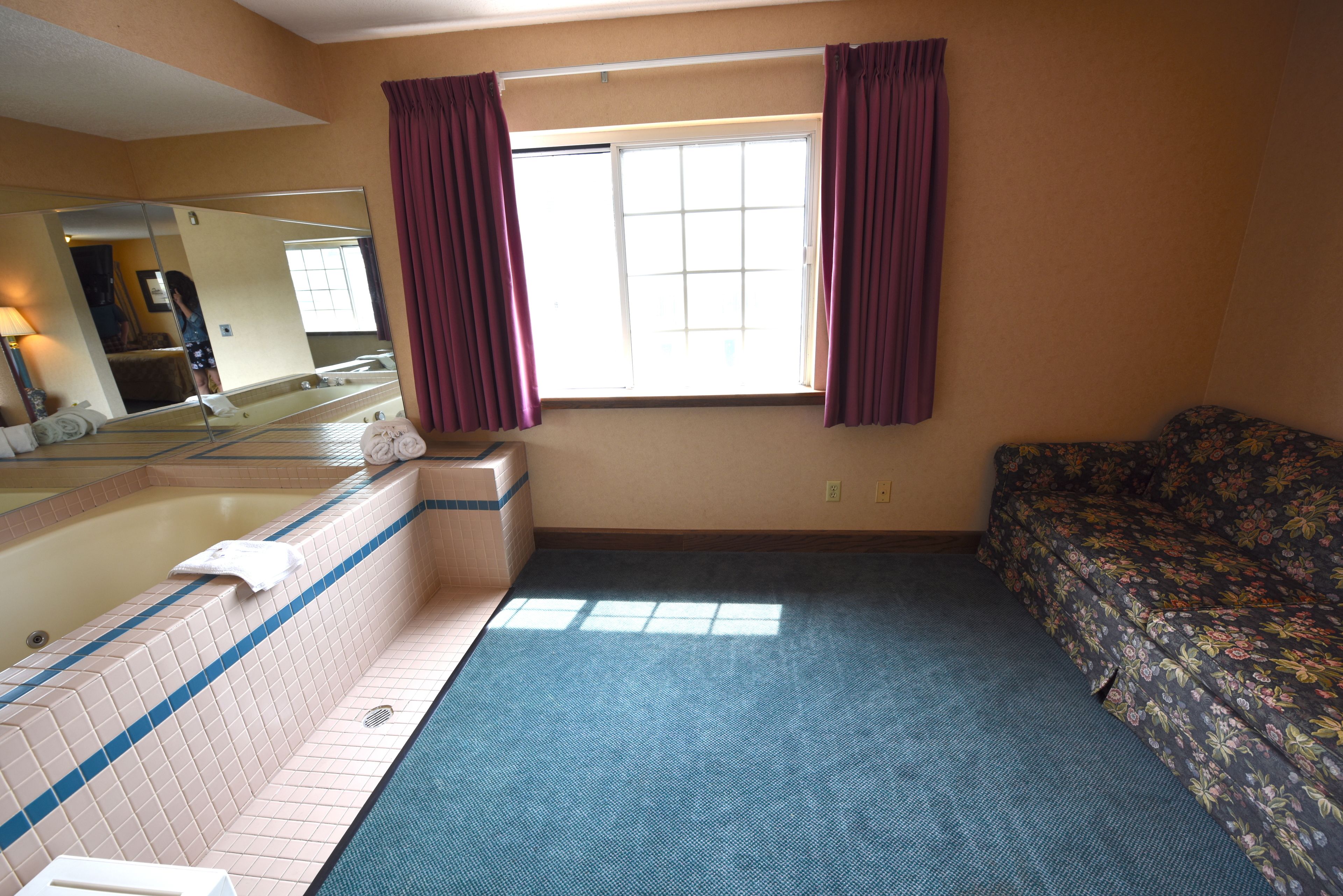 Hotellihuone, jossa on suuri ikkuna, kylpyamme, sohva ja peili.