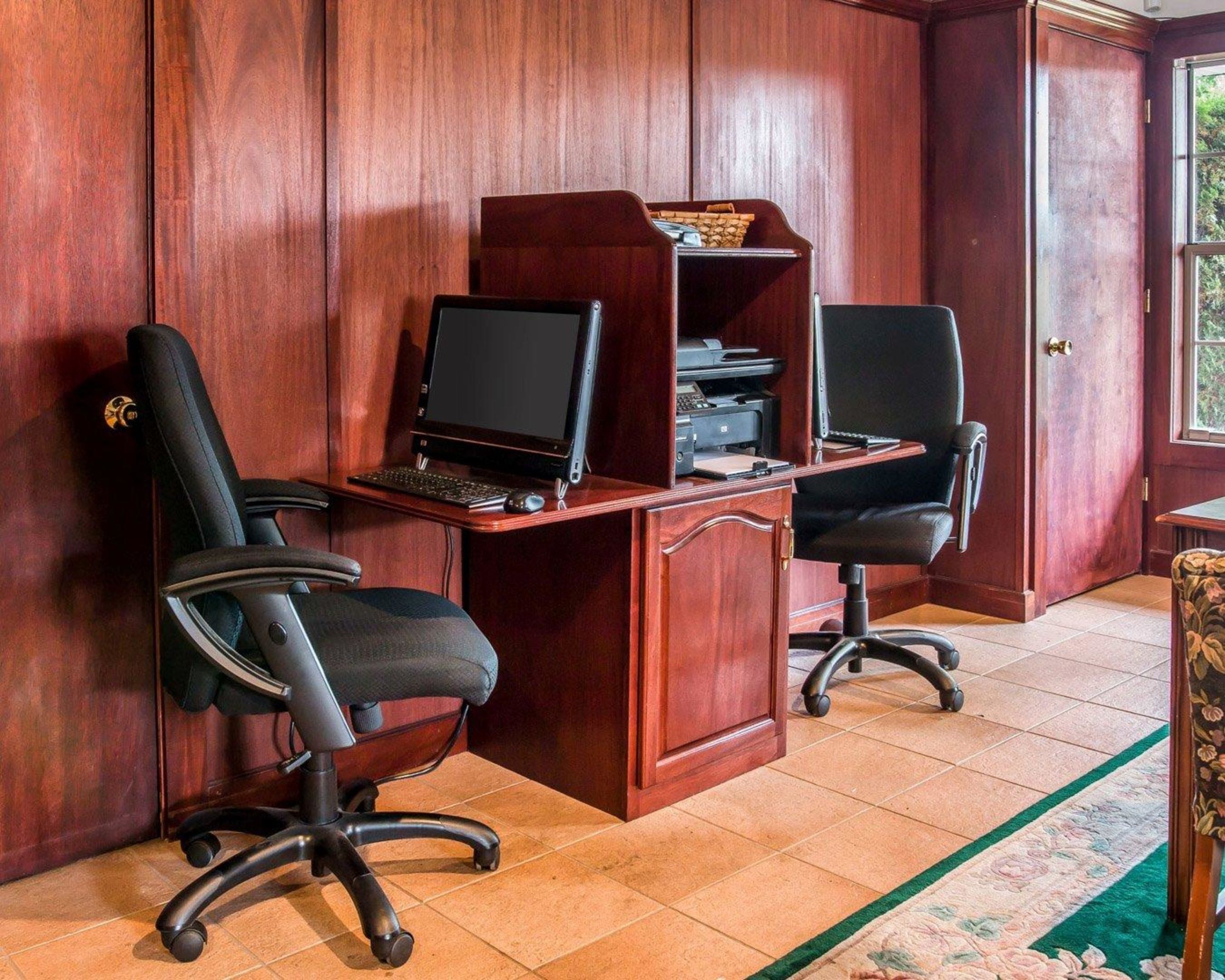 A wooden-paneled room with two black office chairs, a wooden desk with a computer, printer, and shelves.