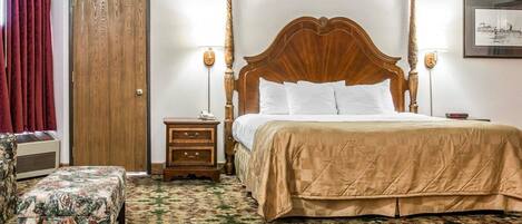 Una cama con dosel y tablero de madera, una mesita de noche con lámpara, un banco estampado con motivos florales y una alfombra con diseño.