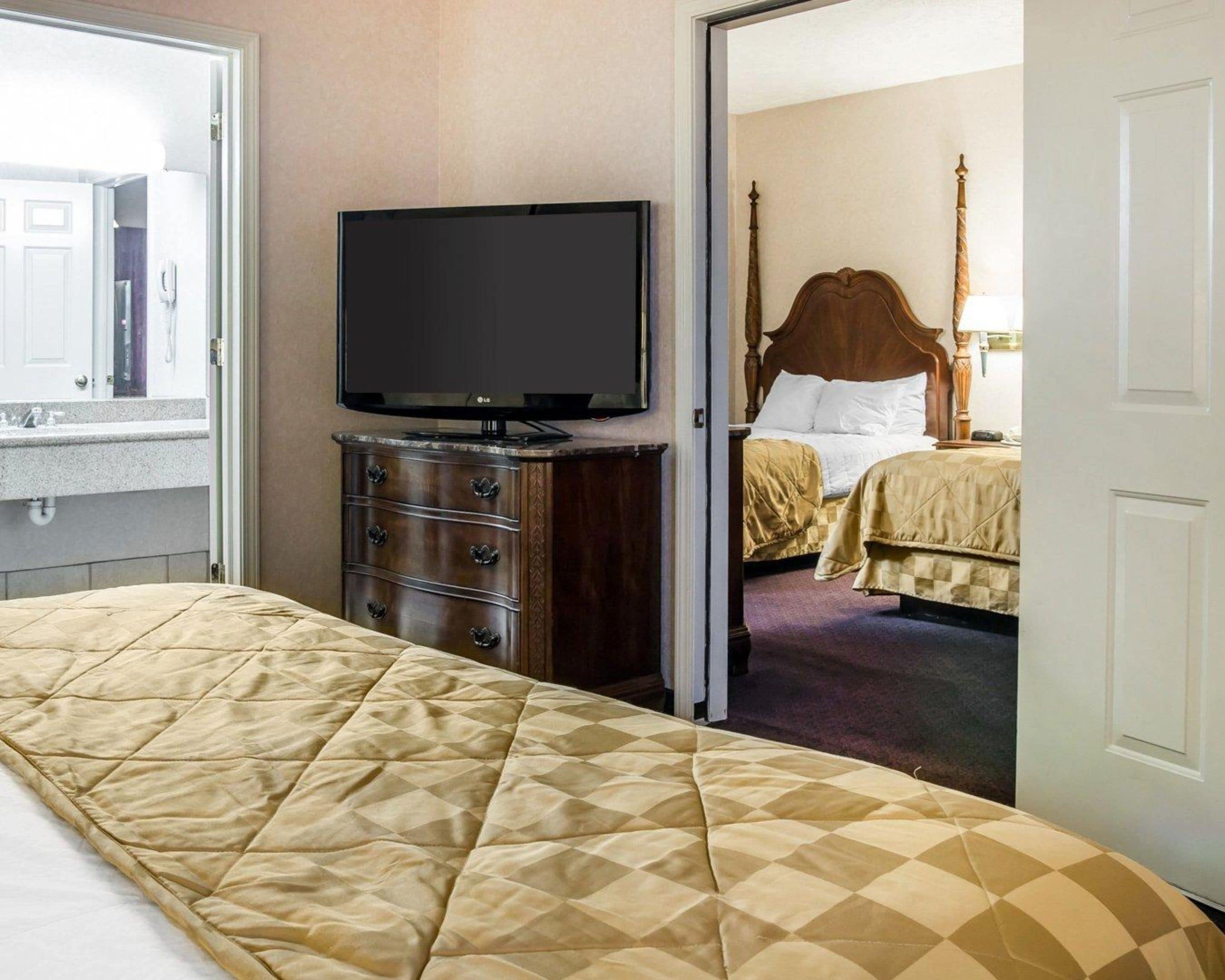 A hotel room with a large bed, a television on a dresser, and a separate bedroom with a bed and nightstand.