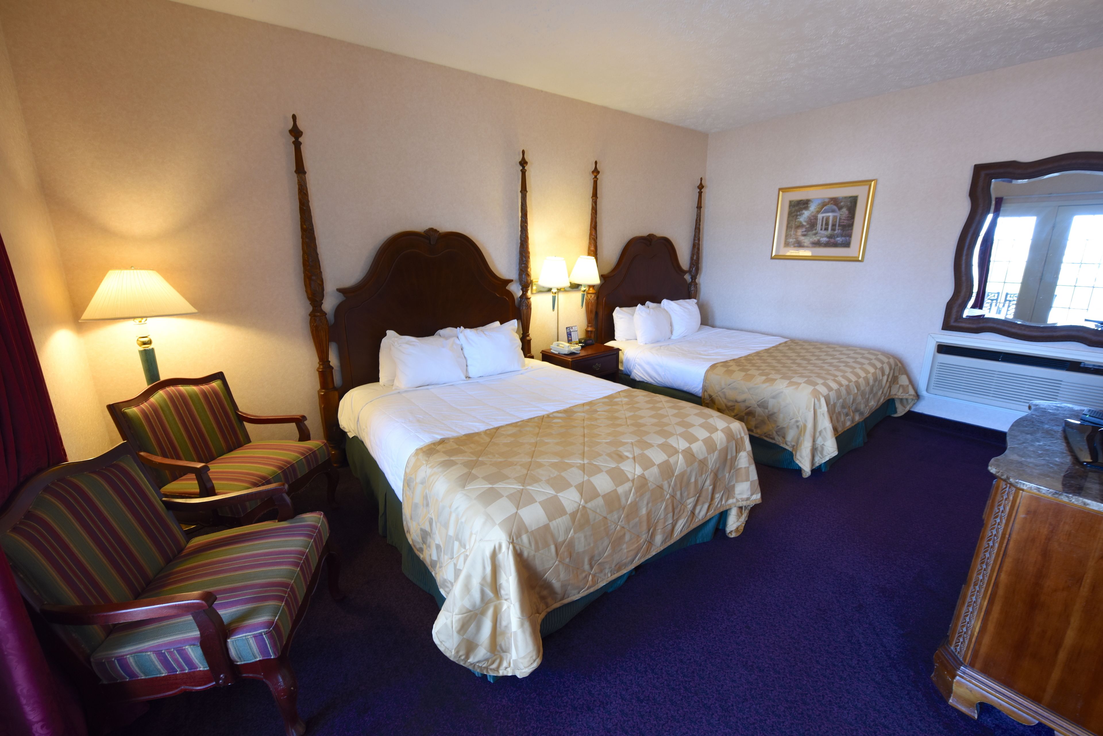 Een hotelkamer met twee bedden, een stoel, een lamp en een schilderij aan de muur.