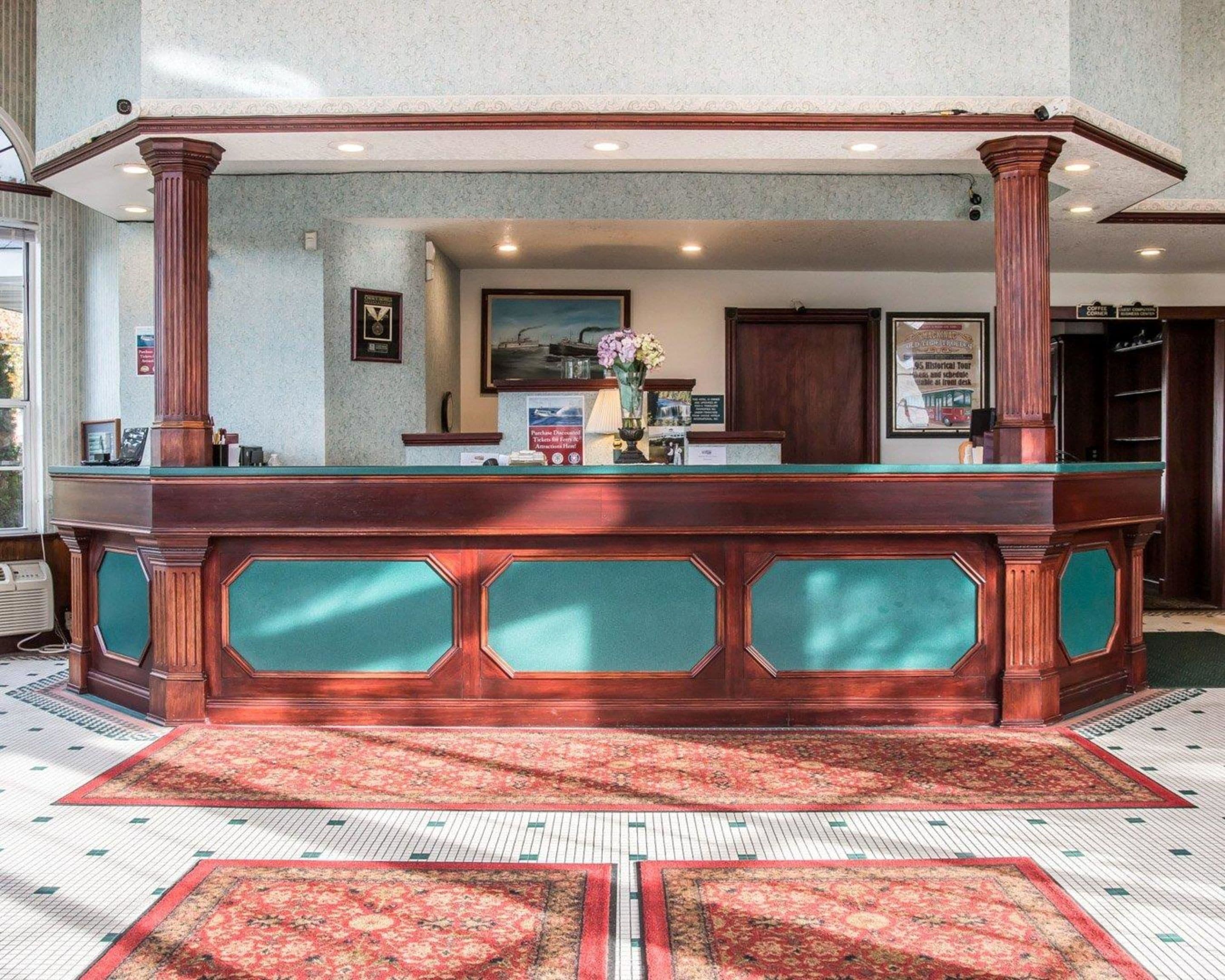 A reception desk with a green cushioned backrest, wooden columns, and a tiled floor with patterned rugs.