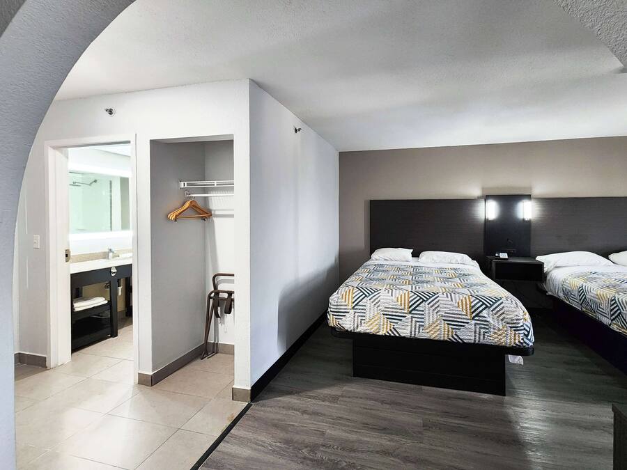 Ett hotellrum med en säng, sängbord, en spegel och ett badrum med en handduksställning.