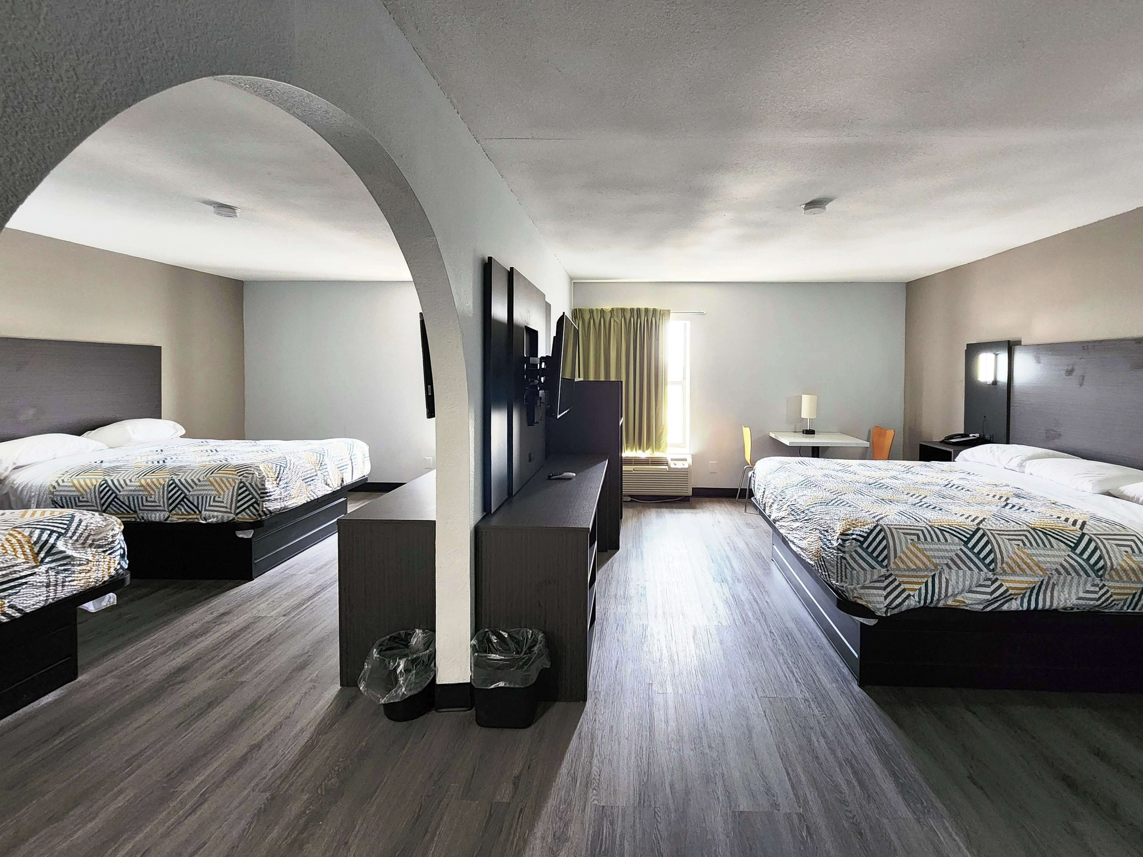 A hotel room with two beds, a TV, a desk, and a window with curtains.