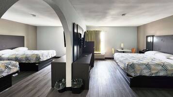 A hotel room with two beds, a TV, a desk, and a window with curtains.